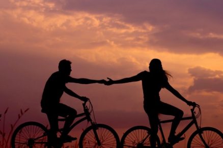 casal andando de bicicleta e dando as mãos